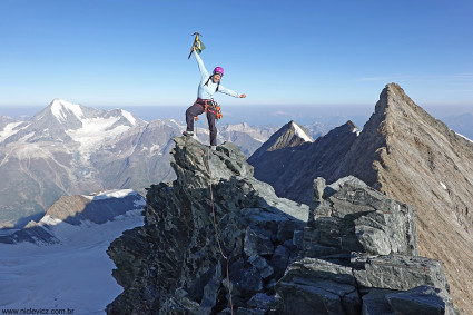 Daiane Luise no cume do Lenzspitze (4.294m). Ao fundo à esquerda, o Weisshorn (4.506m); à direita o cume pontiagudo do Nadelhorn (4.327m), escalado em 2018, mas por onde tivemos que passar para descer. Foto de Waldemar Niclevicz.